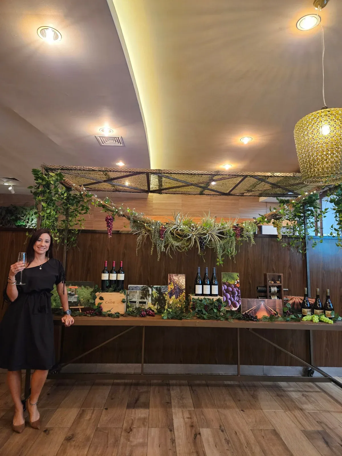 A host with a glass of wine beside the wine display at Root’z