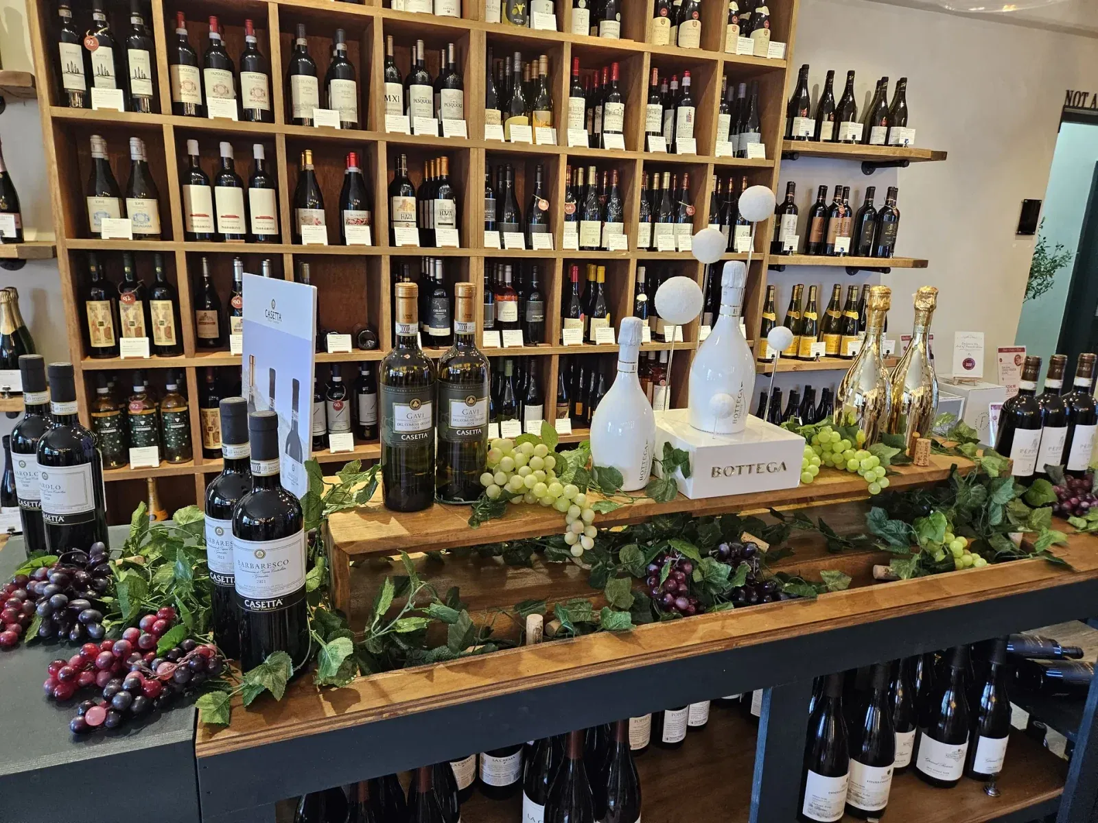 Bottega and Italian wines displayed with grapes and greenery in front of the wine shelves at Provisions Wine & Cheese