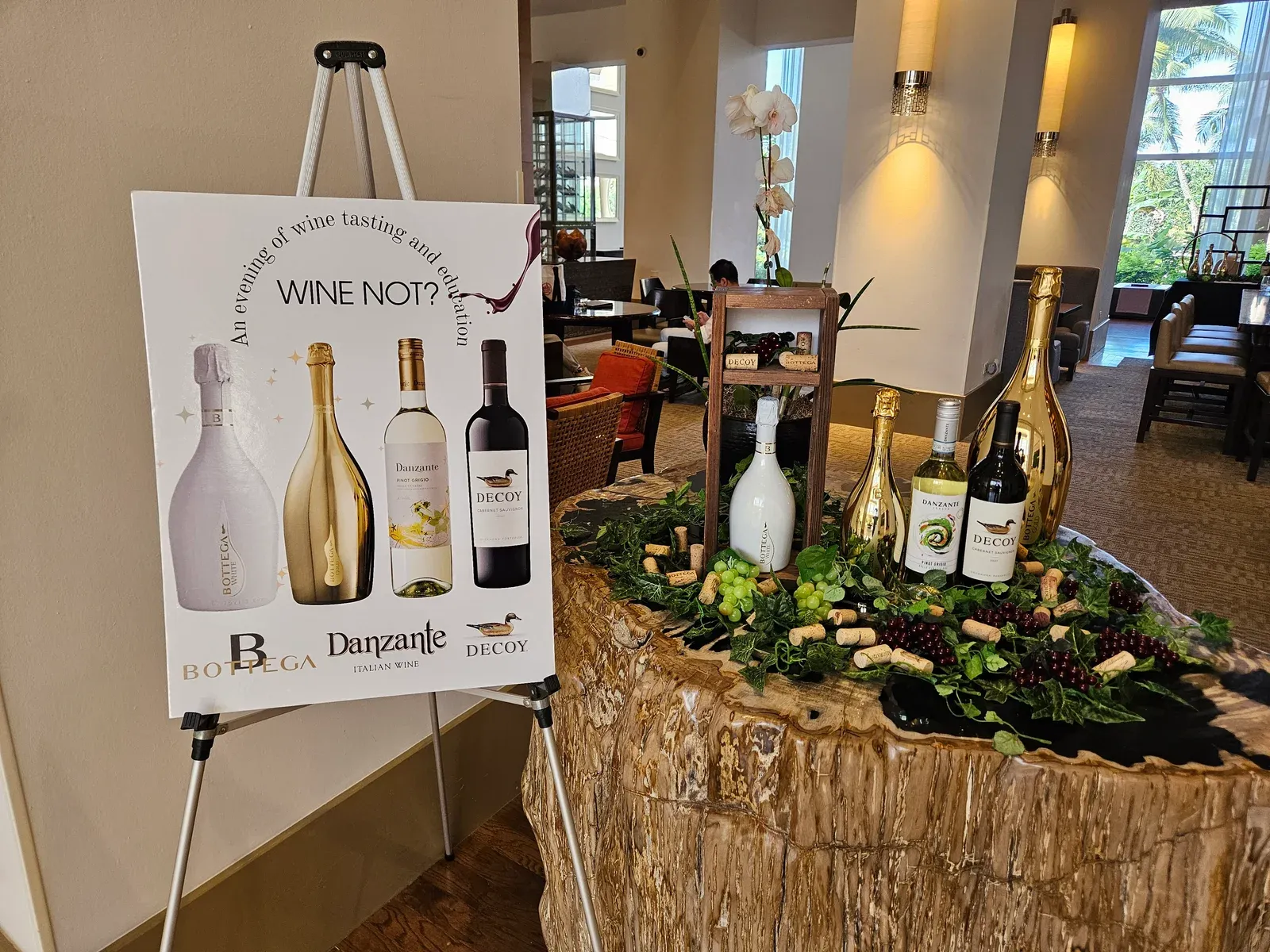 A Wine Not? easel with Bottega, Danzante and Decoy bottles, beside a table dressed with grapes